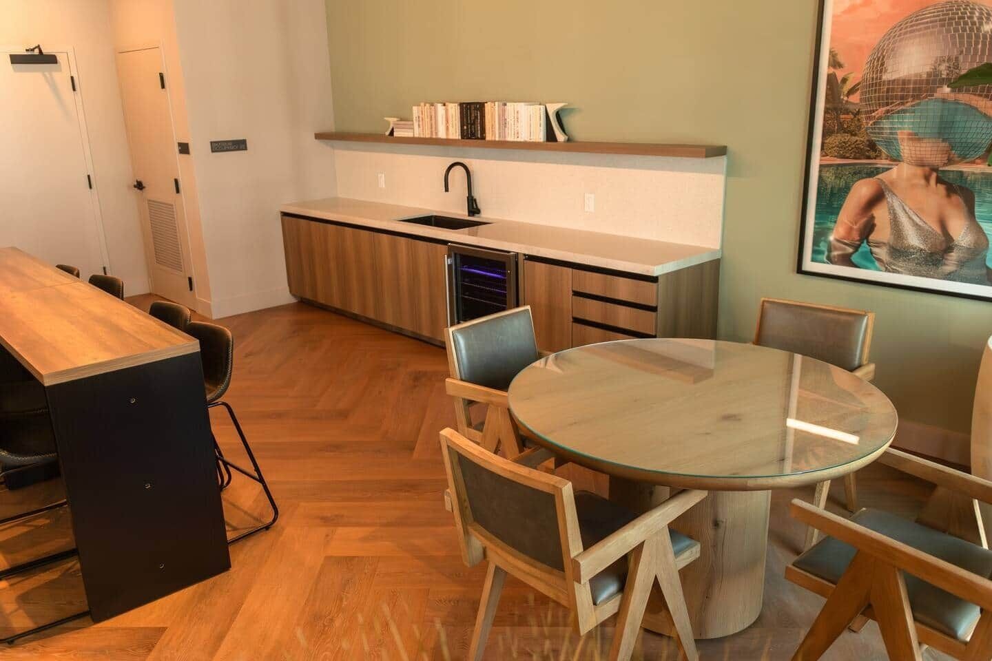 Una cocina moderna con una mesa redonda de cristal y sillas de madera, un lavamanos empotrado y una estantería con libros.