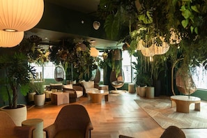 Ein Zimmer mit Holzboden, Korbmöbeln, hängenden Pflanzen und einem großen Fenster.