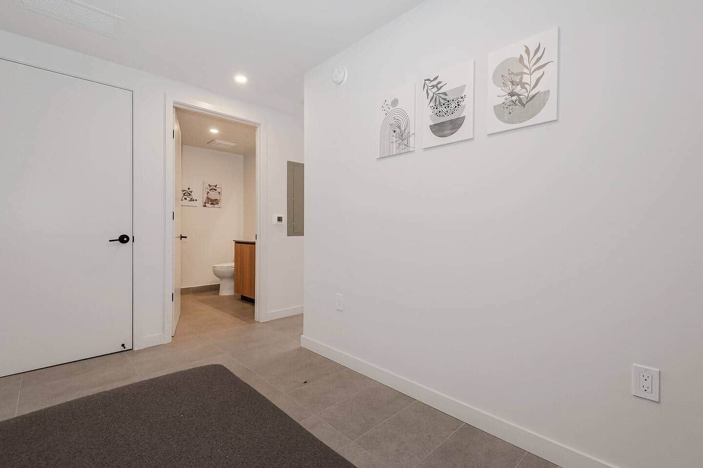 Un couloir avec une porte, un tapis et trois œuvres d’art accrochées au mur.