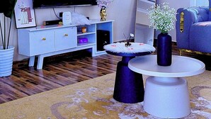 A living room with a flat-screen TV, a white entertainment unit, a round coffee table, and a blue sofa. - We offer peace & serenity…wellcome to our home away from hom (Dar es Salaam)