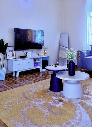 Un soggiorno moderno con una televisione a schermo piatto, un mobile TV bianco, un tavolino rotondo e un divano blu.