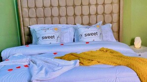 A bed with a tufted headboard, white bedding with 'sweet' pillows, a yellow blanket, and a framed picture on the wall. - We offer peace & serenity…wellcome to our home away from hom (Dar es Salaam)