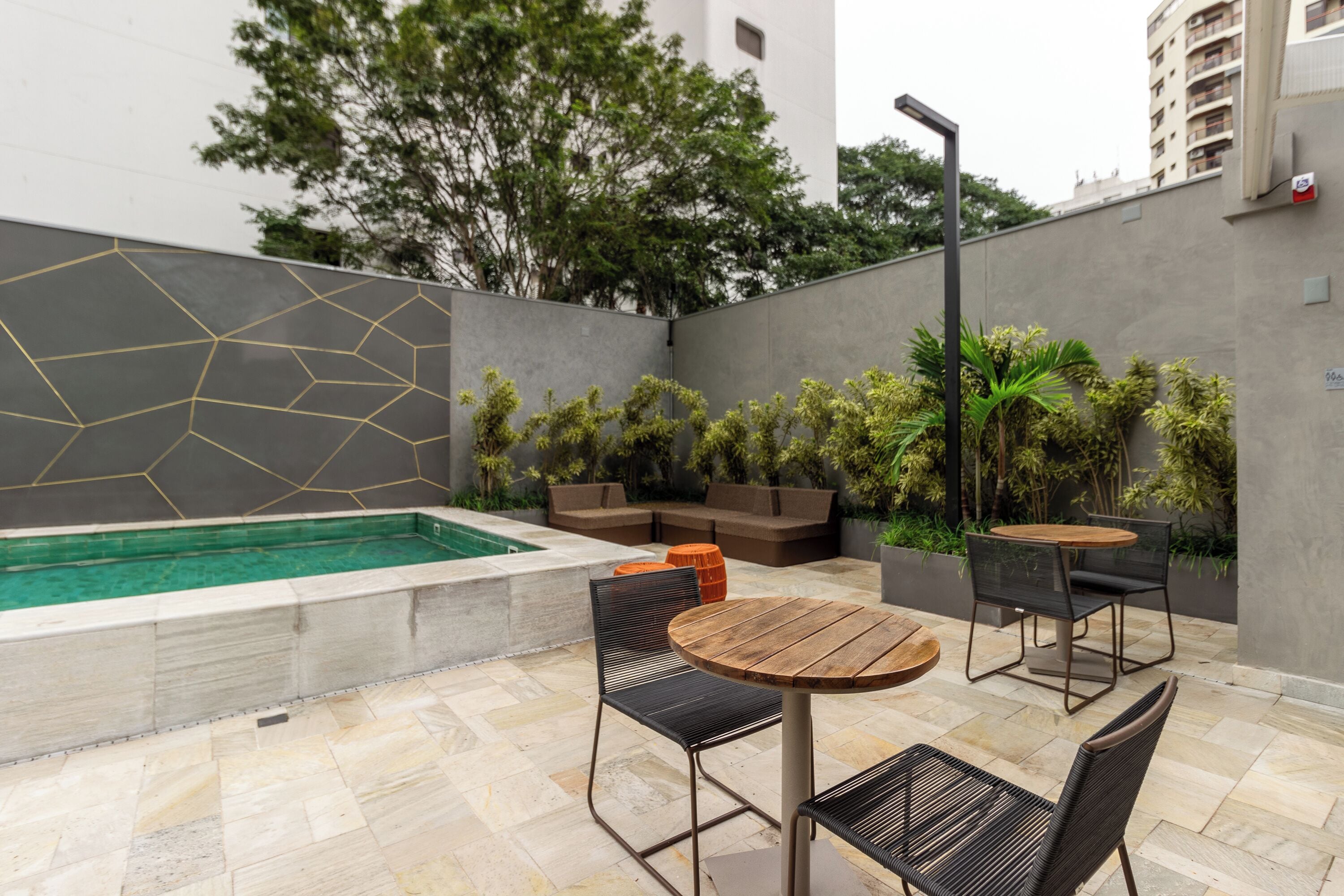 A modern outdoor patio with a pool, seating, and greenery.