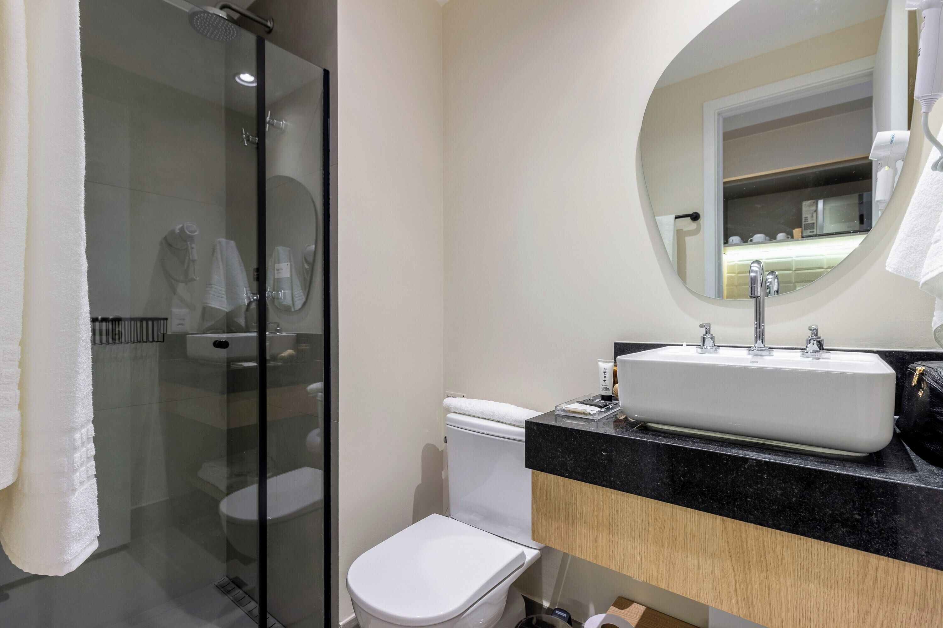 Et moderne badeværelse med en brusekabine i glas, et hvidt toilet, en vask med et spejl over og en håndklæderække.