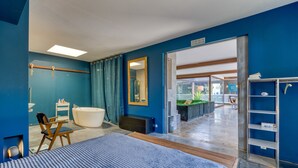 A modern hotel room with a large bed, a bathtub, a vanity with a mirror, and a view into the adjacent room. - Spacious Loft Near the Center with Garden and Pool (Pézenas)