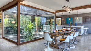 A modern dining area with a large glass wall, a wooden dining table, and contemporary chairs. - Spacious Loft Near the Center with Garden and Pool (Pézenas)