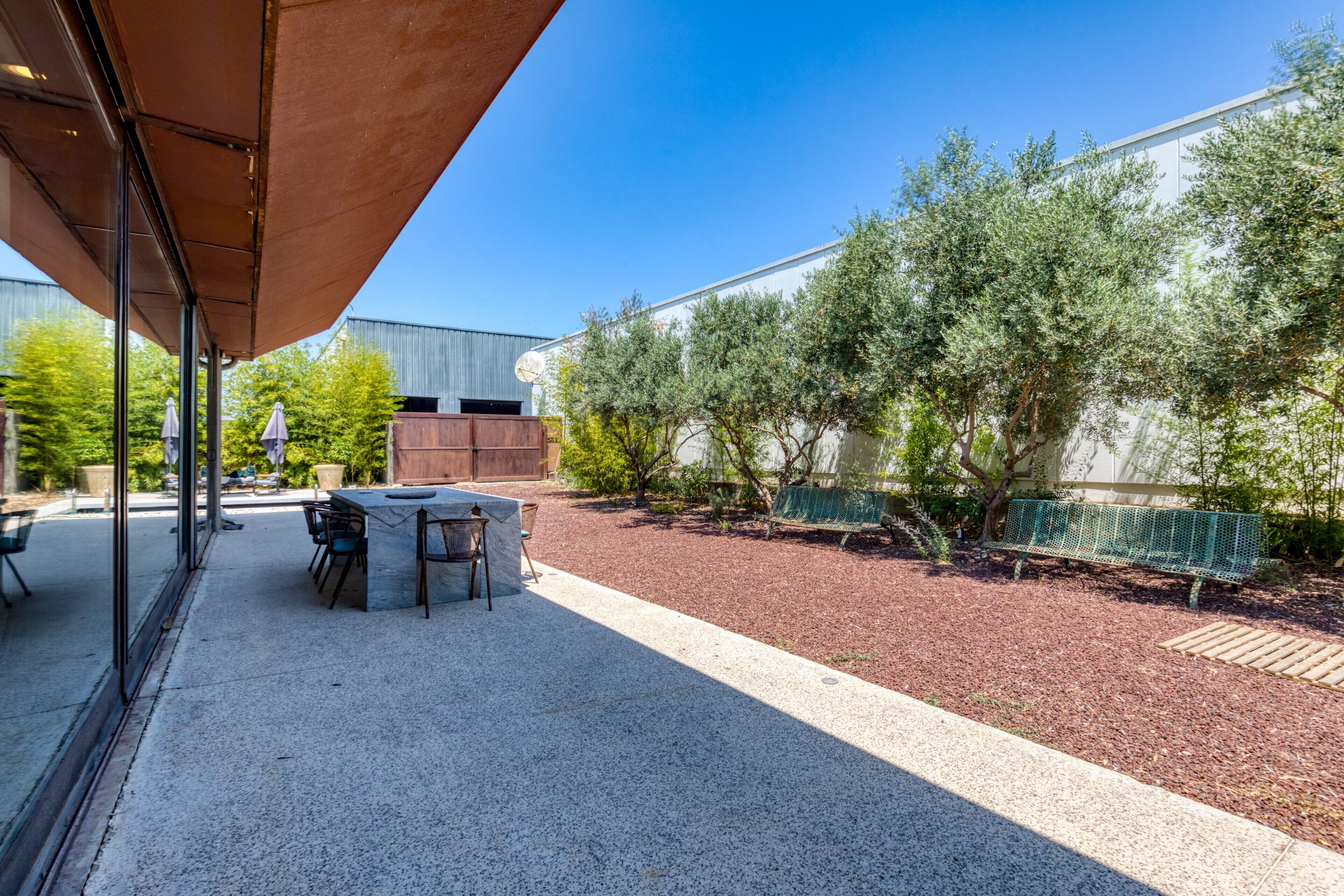 Un patio al aire libre con una mesa y sillas, un espacio de estar techado y un camino de grava que lleva a un edificio.