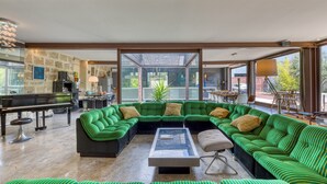 A spacious living area with a green-striped sofa set, a piano, and a large glass door leading to an outdoor patio. - Spacious Loft Near the Center with Garden and Pool (Pézenas)