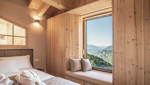 Una habitación con paneles de madera, una cama, un asiento junto a la ventana con cojines y vistas a un paisaje montañoso.