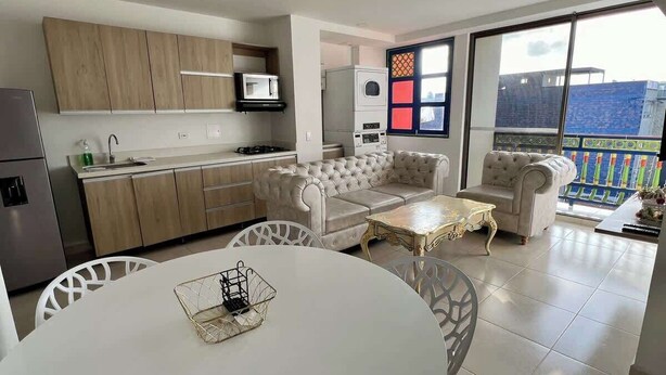 A modern kitchen with built-in appliances, a dining area with a round table and chairs, and a balcony with a view. - Apto Plaza Principal /Vista Embalse/frente Autobús (Guatapé)
