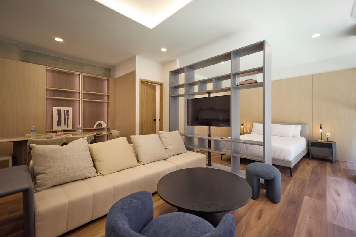 Una habitación de hotel moderna con sofá, una mesa redonda, televisor y cama.