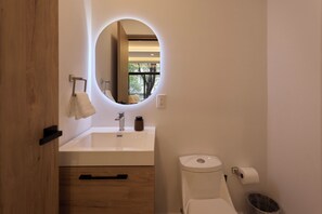 A modern bathroom with a round mirror, a sink, a toilet, and a trash can. - Oniria Living  Free Parking & Rooftop (Mexico City)