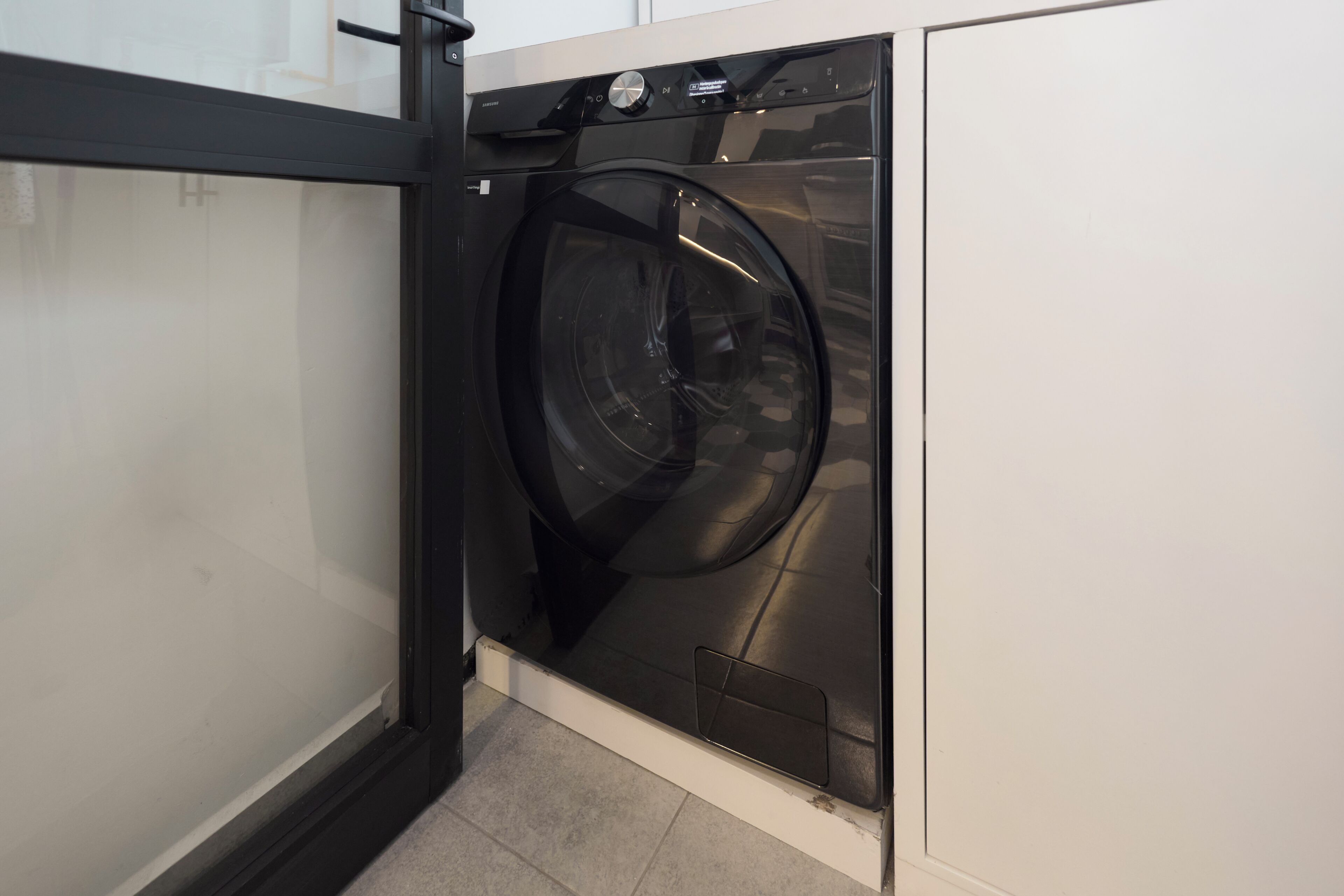A compact, modern laundry room with a built-in washer and dryer, a small control panel, and a tiled floor.