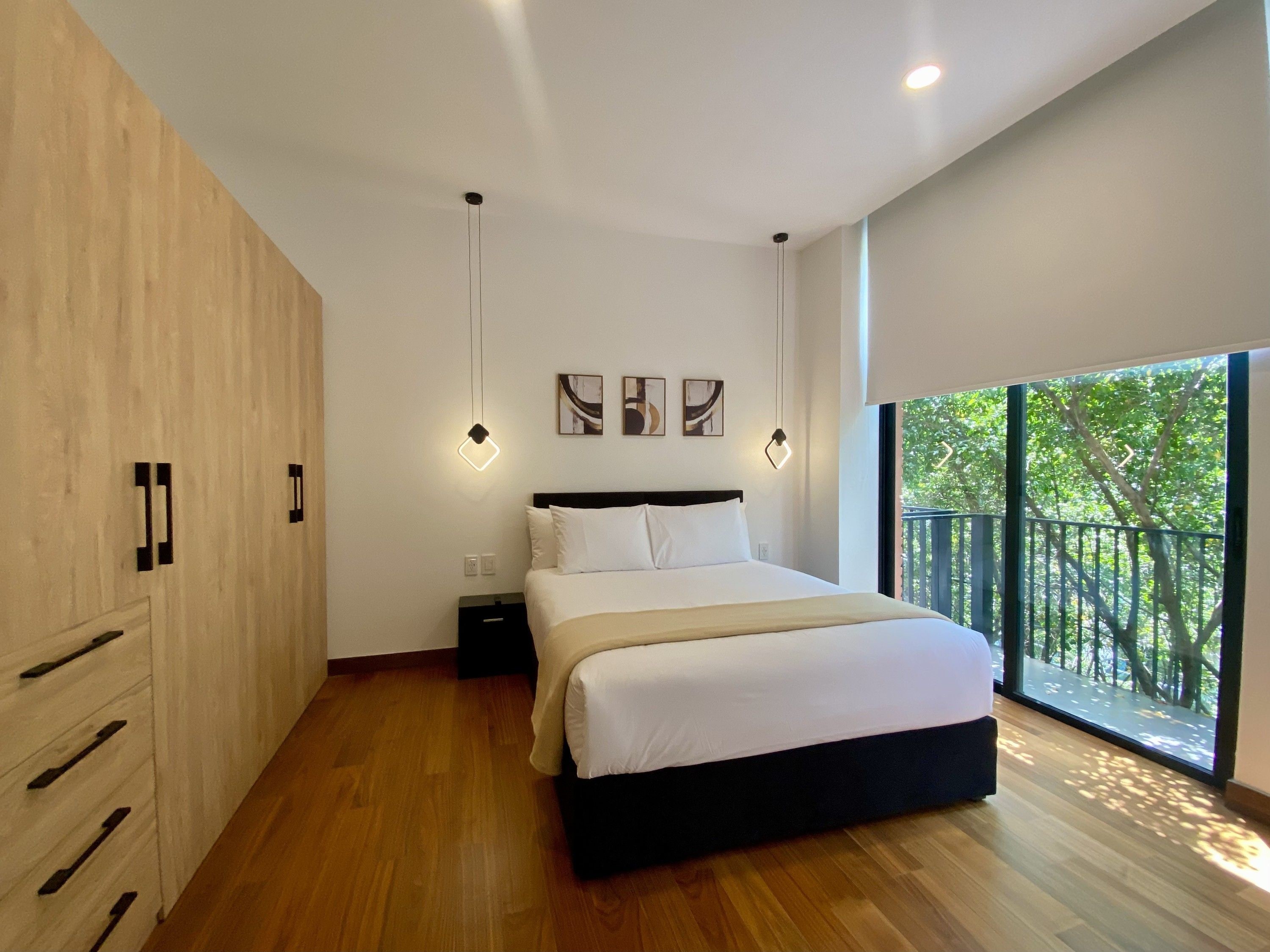 A modern bedroom with a large bed, wooden wardrobe, and a view of trees through a large window.