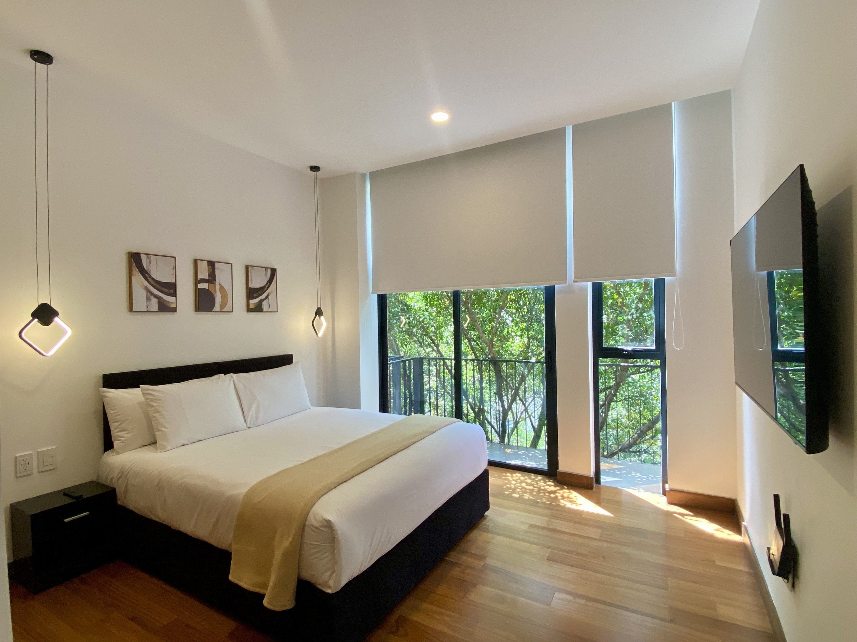 Un dormitorio moderno con una cama grande, una televisión de pantalla plana y un balcón con vista a árboles.