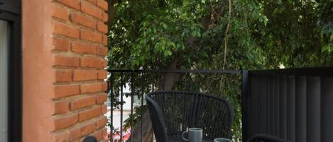 A balcony with a brick wall, a wicker chair, and a table with two cups.