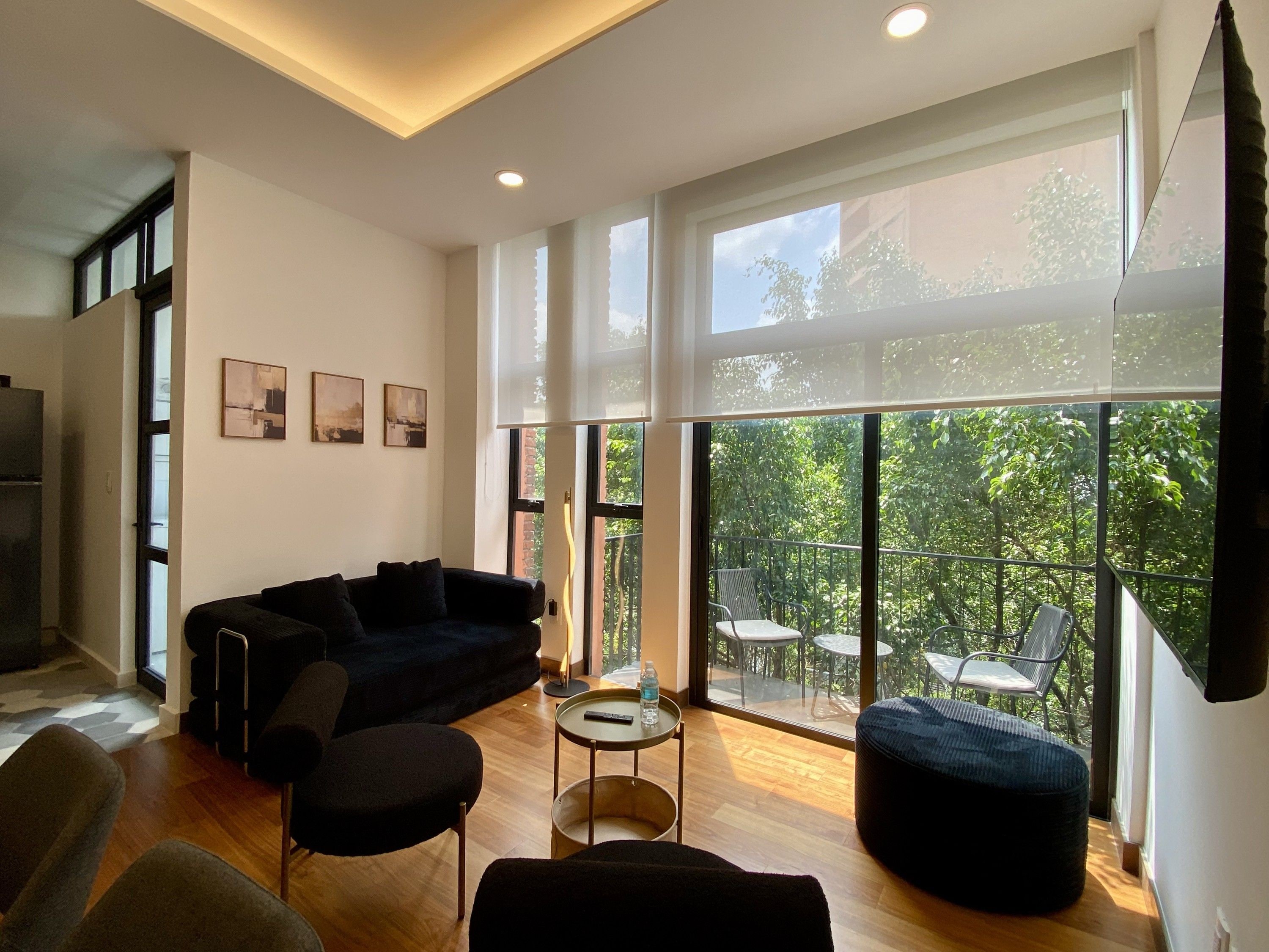 Een moderne woonkamer met een bank, stoelen, een bijzettafeltje en grote ramen met uitzicht op groen.