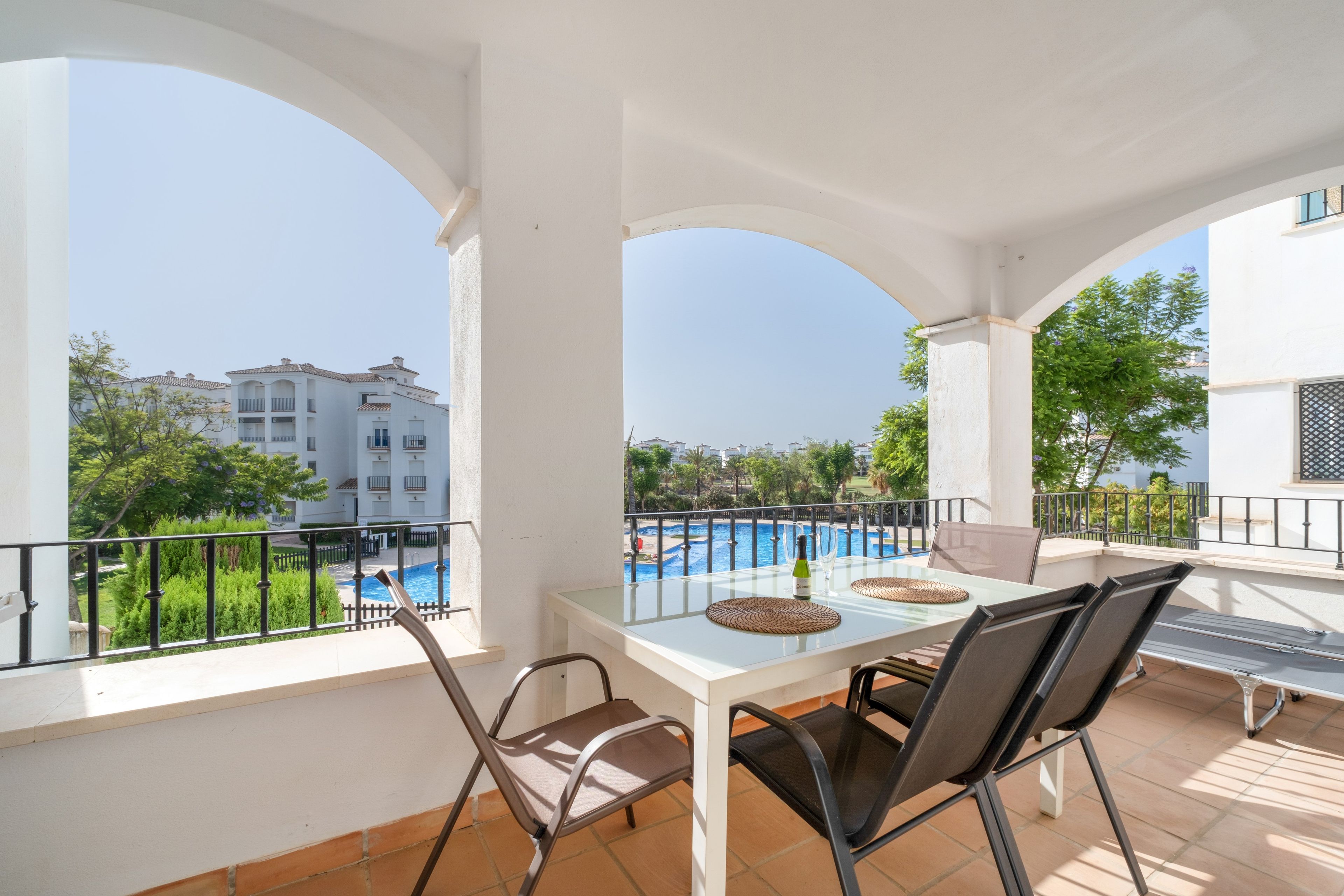 Una terraza con una mesa y sillas, con vista a una piscina y un edificio al fondo.