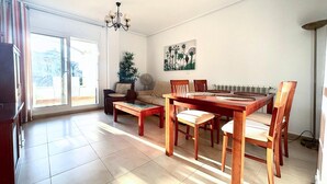 Un salon spacieux comprenant un coin repas, de grandes fenêtres, un lustre et un radiateur.