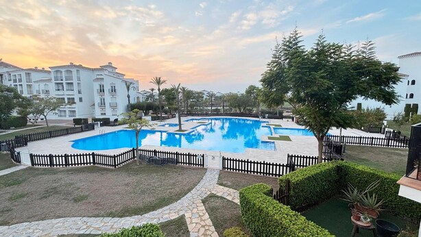 Une piscine entourée d’une clôture, avec un bâtiment en arrière-plan.