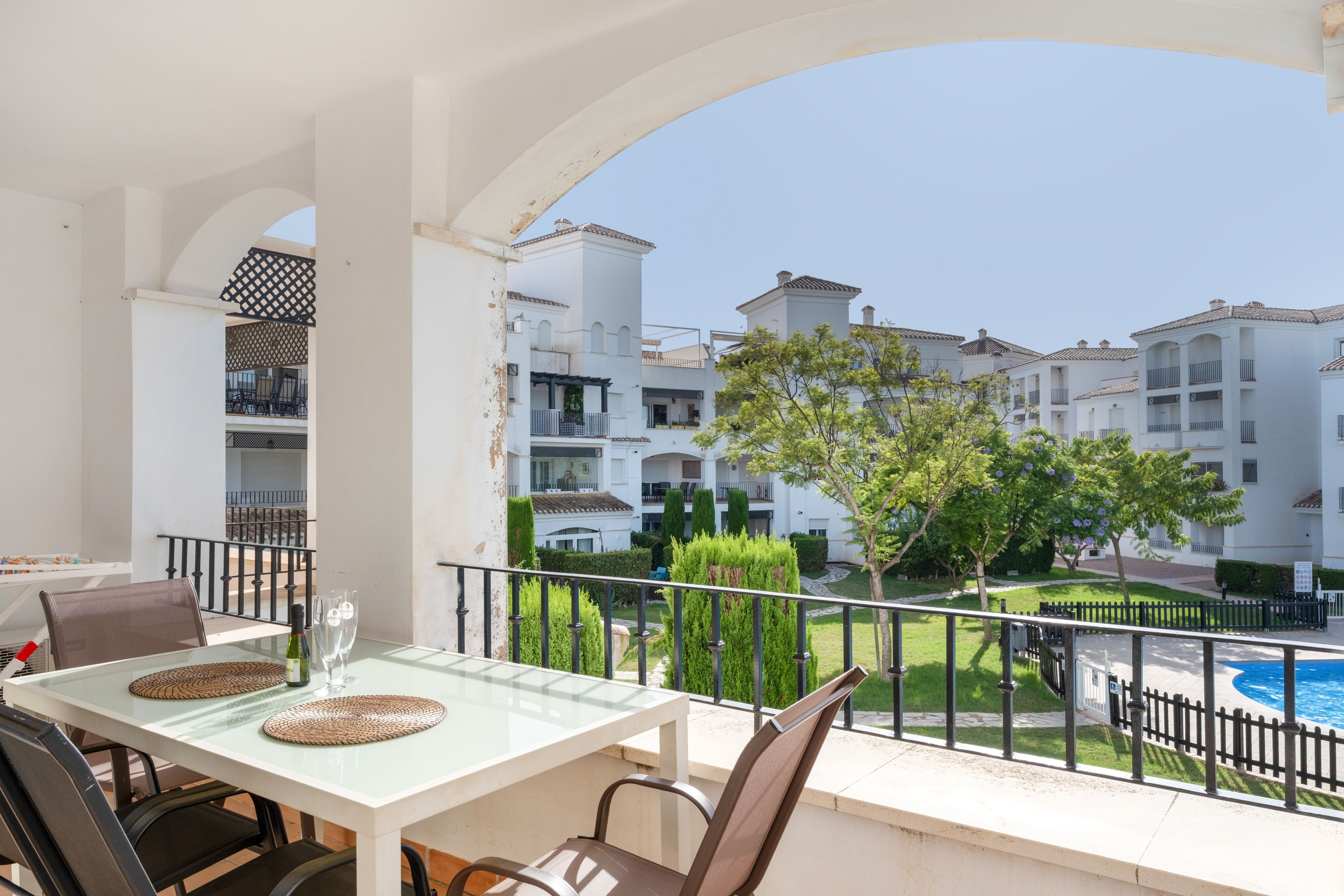 Un balcón con mesa y sillas, con vista a una piscina y edificios residenciales.