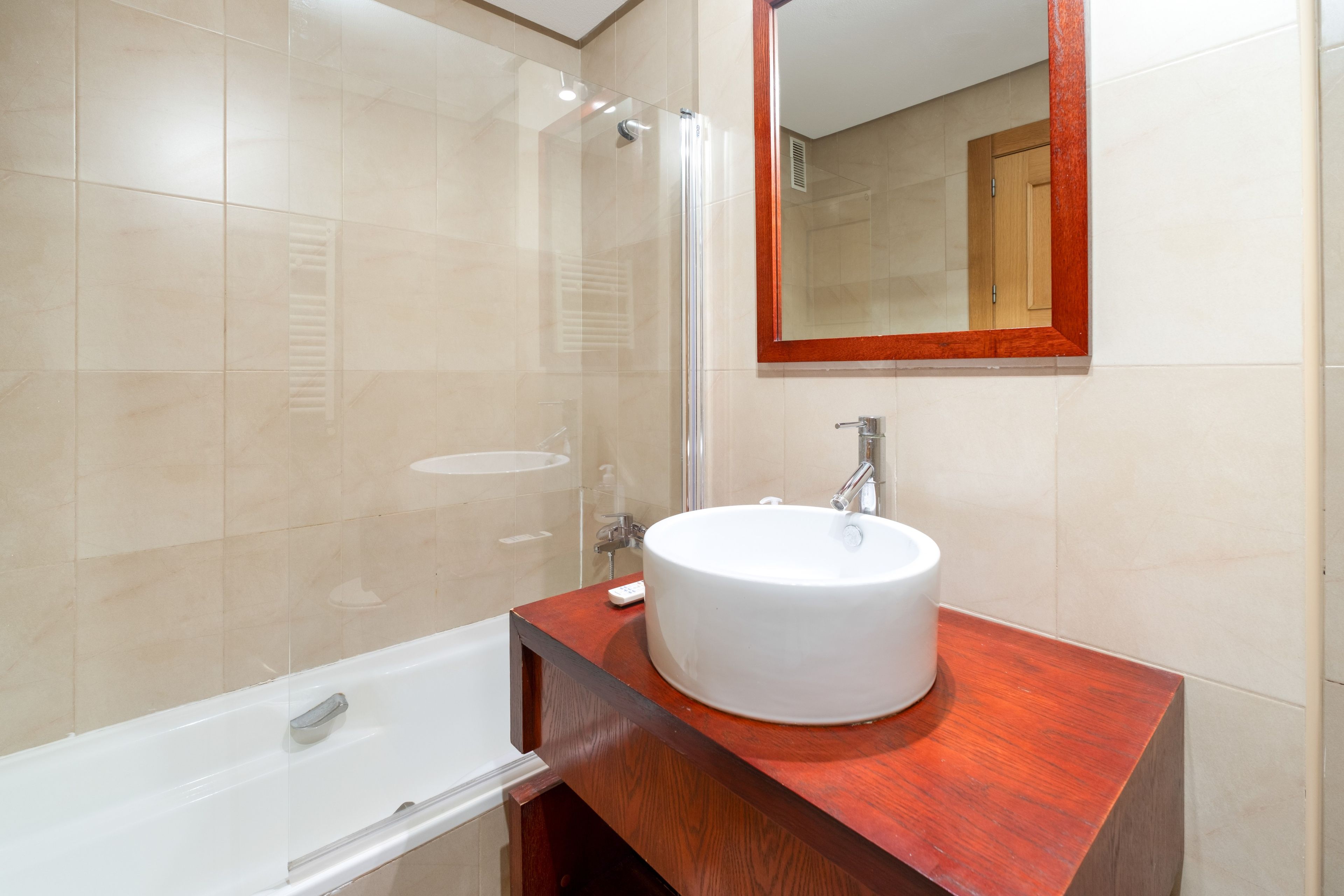 Un baño con una bañera blanca, un lavabo redondo y una ducha con mampara de cristal.