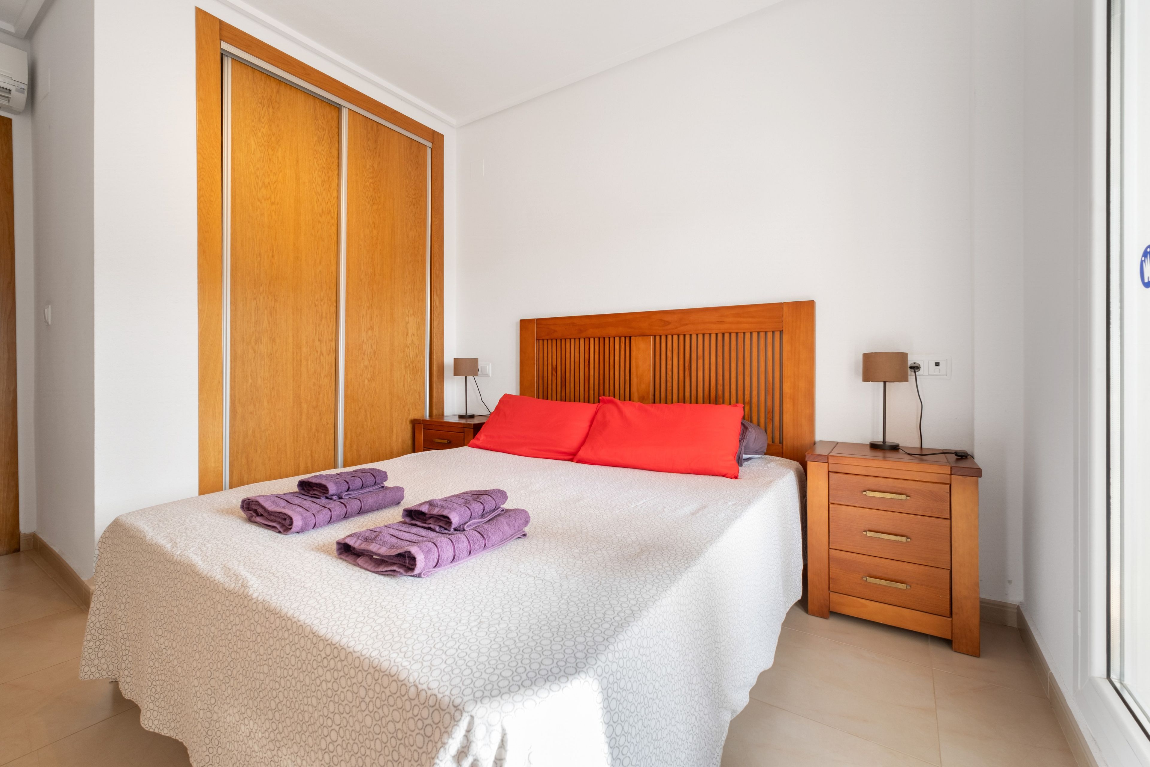 Una habitación de hotel con una cama, una mesita de noche, una lámpara y un armario.