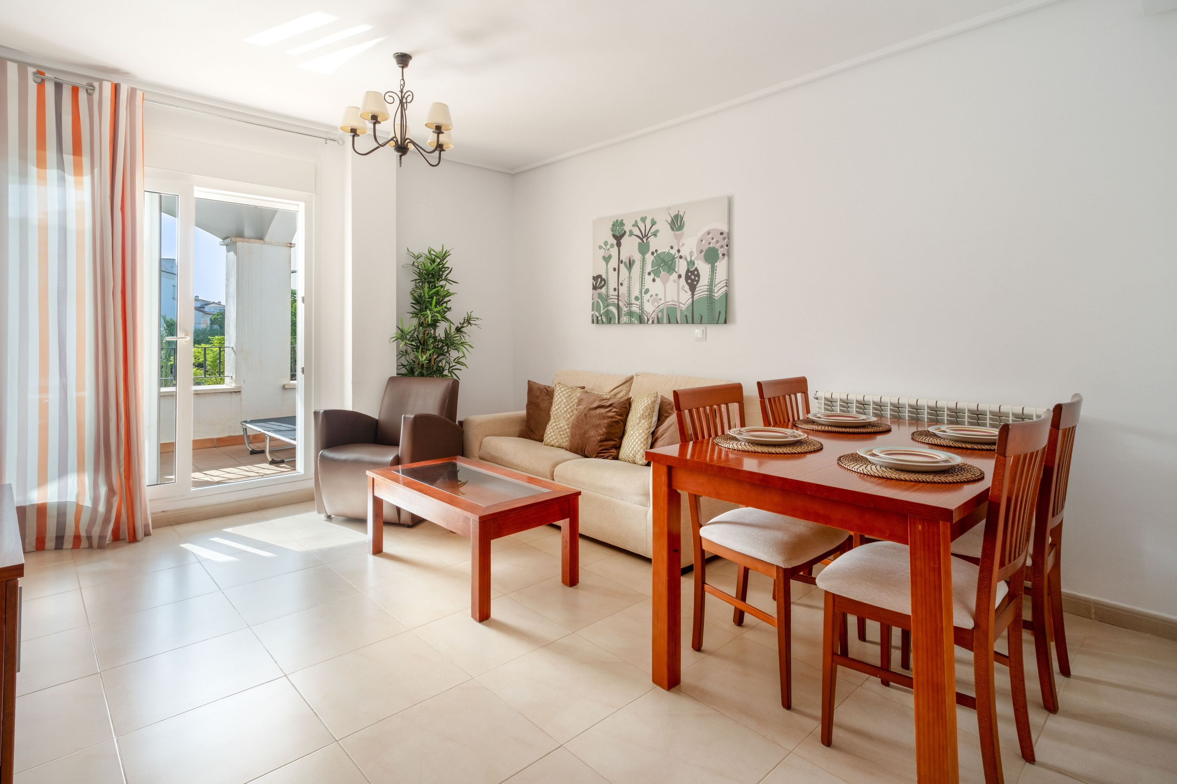 A modern living room with a sofa, coffee table, dining table with chairs, a potted plant, and a painting on the wall.