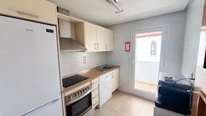 Une cuisine équipée d’un réfrigérateur, d’une cuisinière, d’un four et d’un évier. Une fenêtre offre une vue sur l’extérieur.