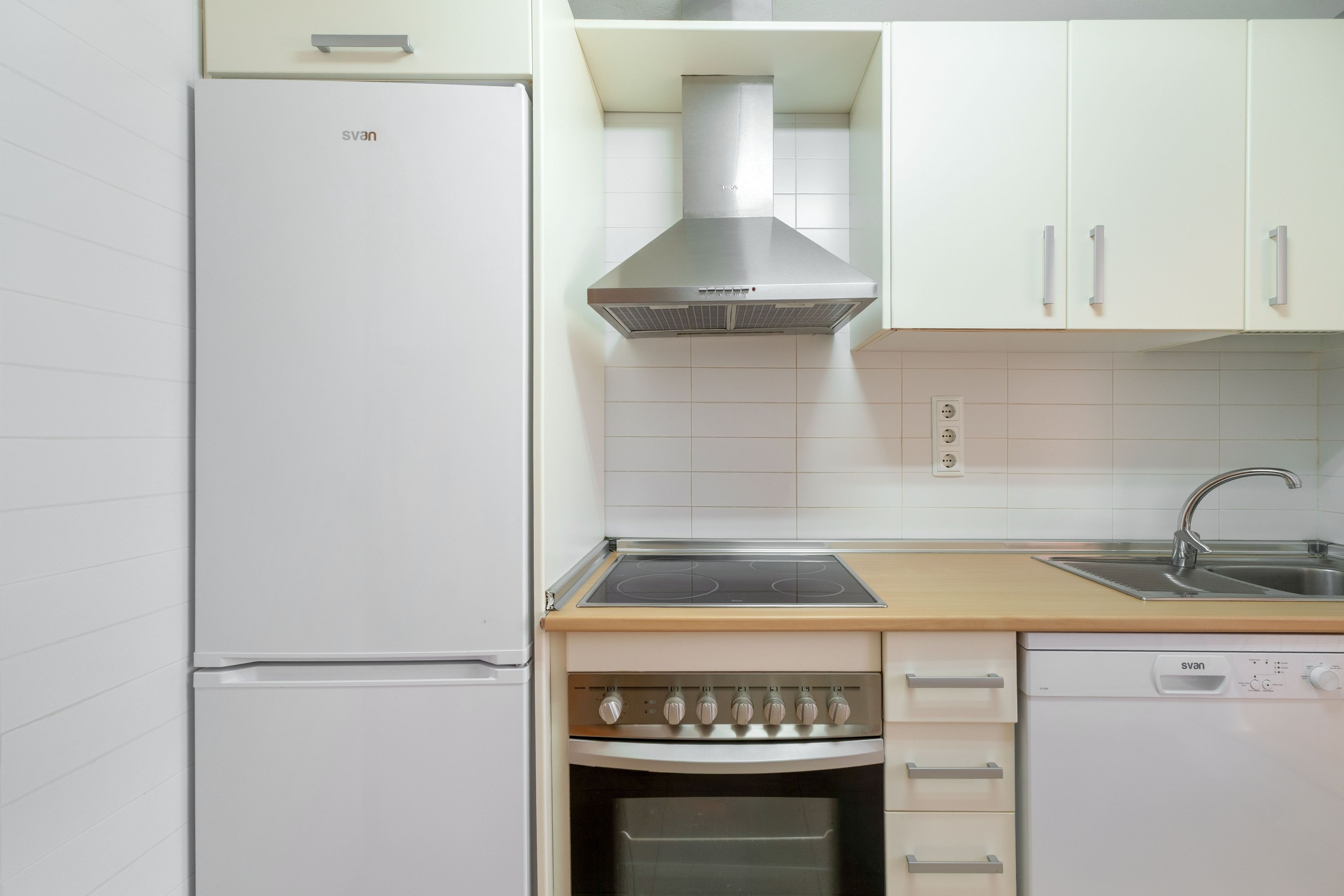 Cocina compacta con horno empotrado, extractor de acero inoxidable y lavavajillas.