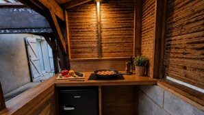 Ett kompakt kök med träväggar, ett inbyggt kylskåp och en liten arbetsyta med köksredskap och en stekpanna.