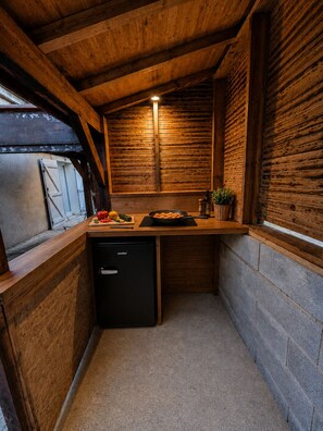 A compact kitchen with wooden walls, a built-in refrigerator, and a small countertop with cooking utensils and a pan. - "Chez papi Rob", Landes house with pétanque court, a stone's throw from the center. (Andernos-les-Bains)