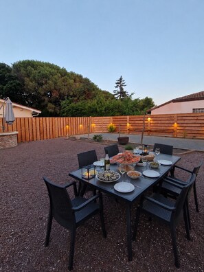 An outdoor dining area with a table set for six, surrounded by chairs, and a wooden fence in the background. - "Chez papi Rob", Landes house with pétanque court, a stone's throw from the center. (Andernos-les-Bains)