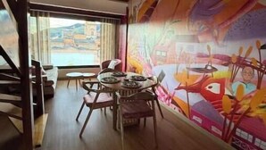 A dining area with a table and chairs, a mural on the wall, and a view through a window. - Historic Downtown - Modern Loft - Toque Cocha - Quillak (Nariño)