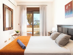 Ein Hotelzimmer mit Bett, einem Vorhangfenster, einem kleinen Tisch mit Pflanze und Blick ins Freie.