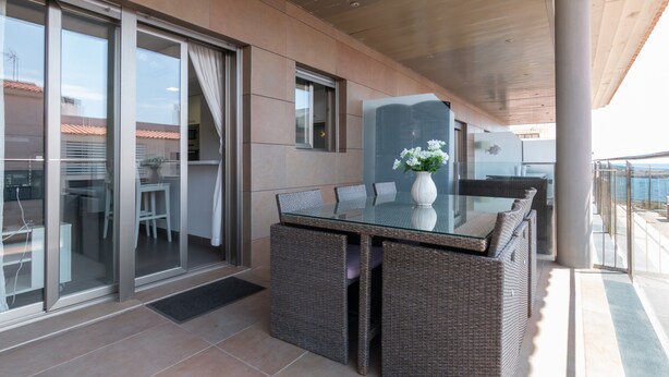 Un balcon avec une table en verre et des chaises en osier, une porte-fenêtre coulissante et une vue sur la mer.