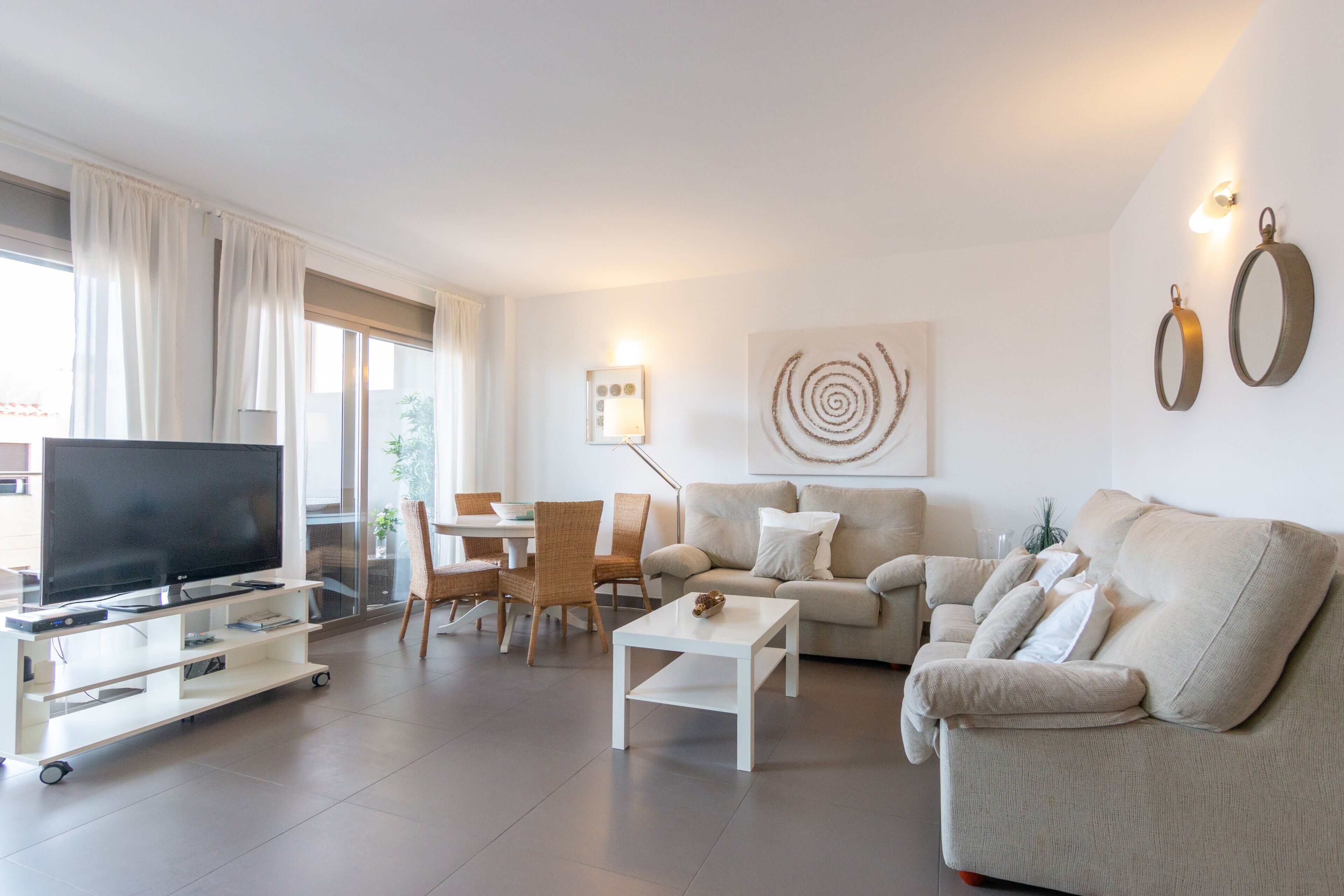 A modern living room with a flat-screen TV, a sofa, a coffee table, and a dining area with chairs.