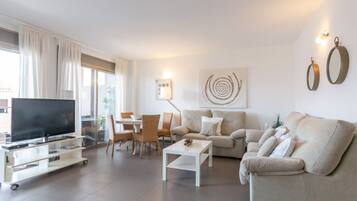 A modern living room with a flat-screen TV, a sofa, a coffee table, and a dining area with chairs.
