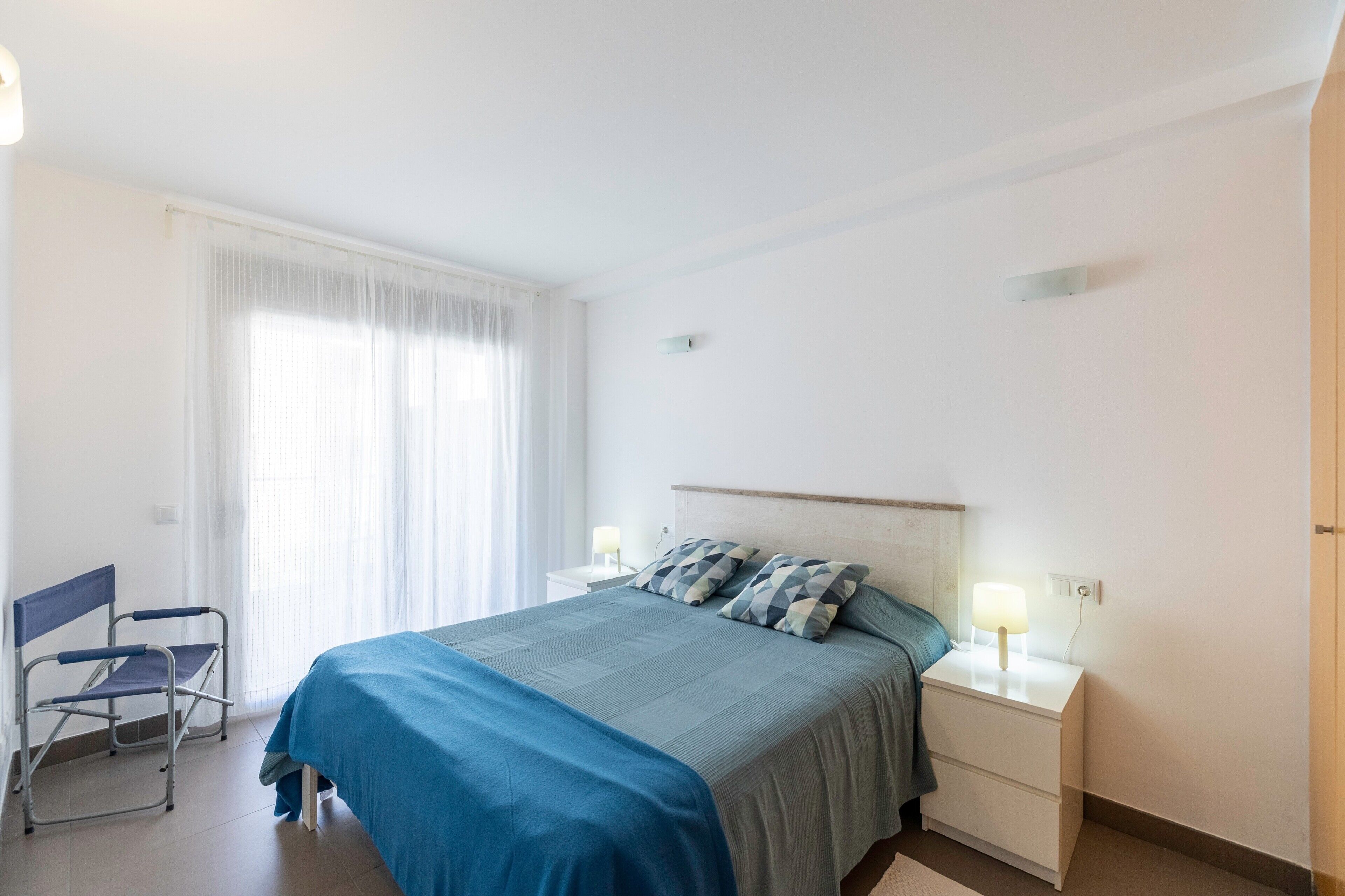 A bedroom with a bed, nightstands, a chair, and a window with curtains.