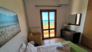 Ein Schlafzimmer mit Bett, Sessel, Kommode, Spiegel und Blick ins Freie.