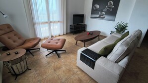 Ein Wohnzimmer mit braunem Ledersessel, beiger Couch, rundem Couchtisch, einem kleinen Beistelltisch und einem Fernsehschrank.