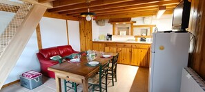 A dining area with a wooden table set for four, a red sofa, and a kitchen with wooden cabinets and a refrigerator.