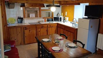 Ein Holzblockhaus-Interieur mit einem Esstisch, gedeckt für vier Personen, einer Küche mit Mikrowelle und Toaster sowie einem an der Wand montierten Fernseher.