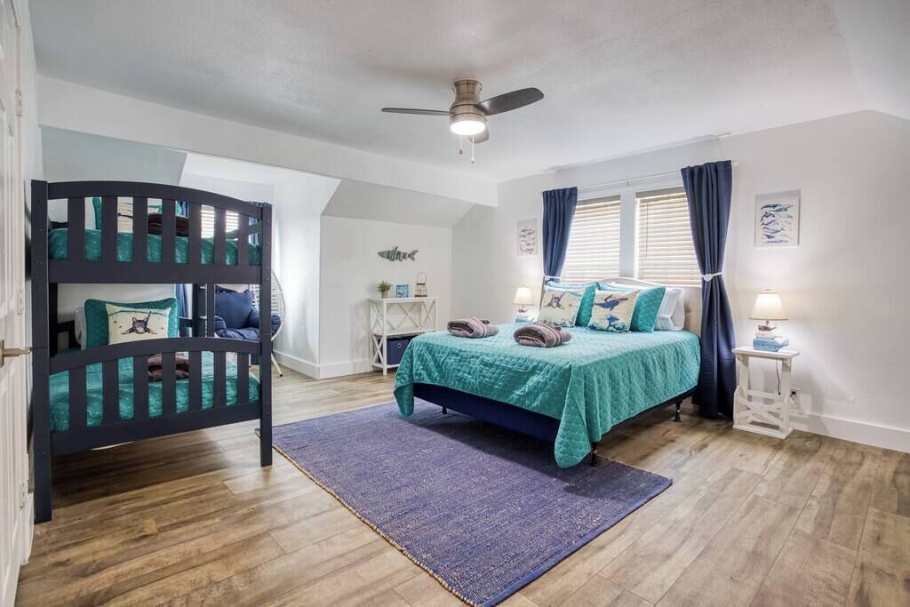 A bedroom with a bunk bed, a single bed, a ceiling fan, and a window with curtains.