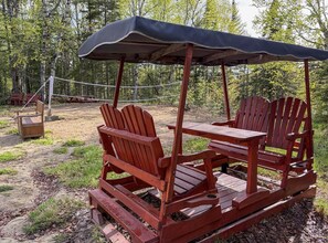 Un set con sedia e tavolino Adirondack in legno, riparato da un gazebo in una zona boschiva.