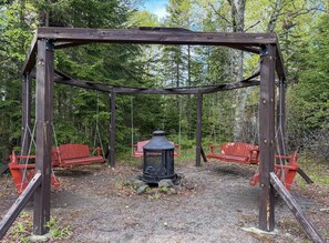 Un’altalena in legno con panchine, un lampione al centro e uno sfondo boschivo.