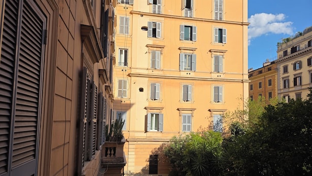 A narrow alleyway flanked by multi-story buildings with balconies and shutters.