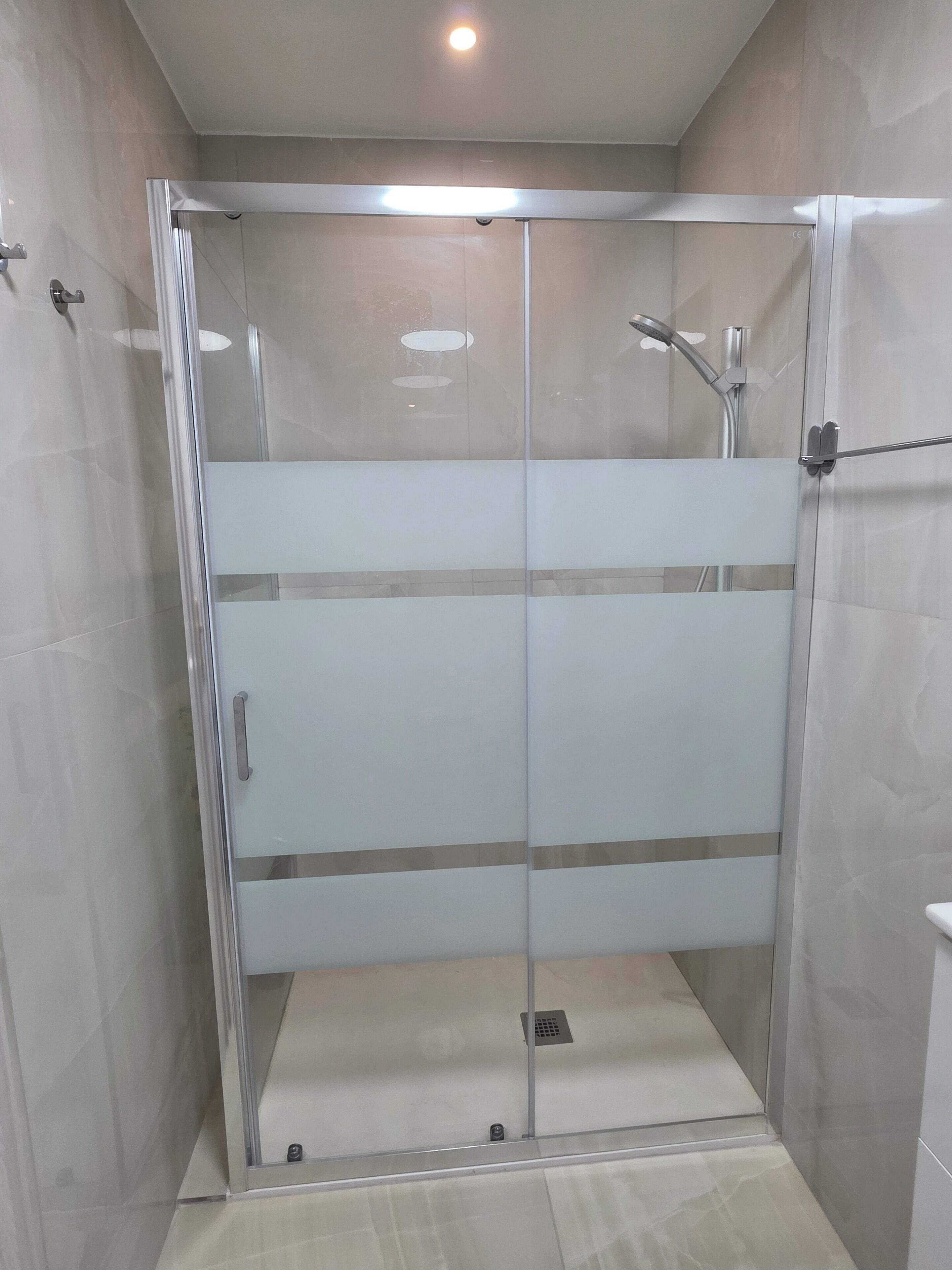 A glass-enclosed shower stall with a tiled floor and a ceiling light.