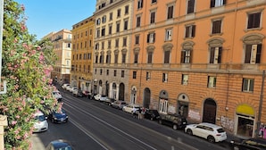 A multi-story building with a row of parked cars and a tram line running down the street.