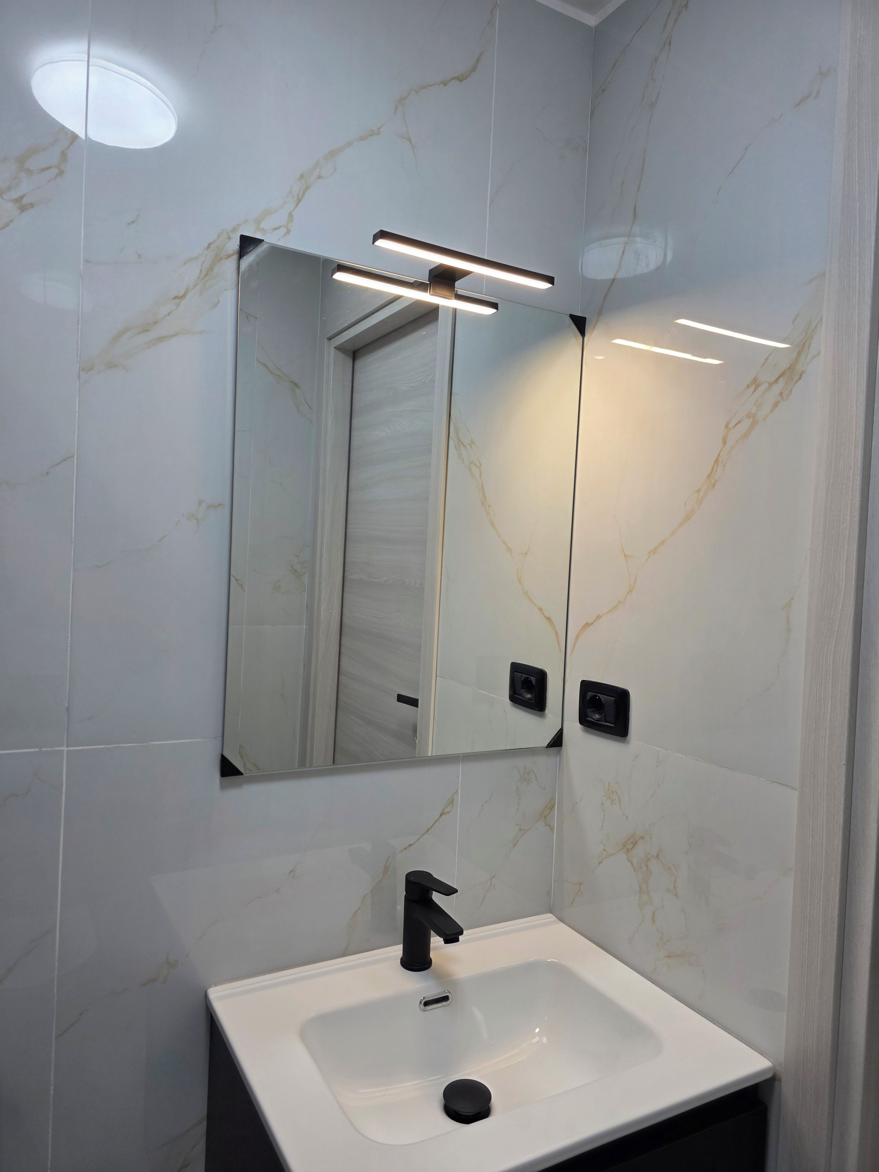 A bathroom with a white sink, a mirror, and a modern light fixture.